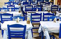 Empty Greek taverna tables and blue chairs.