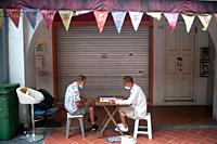 Singapore, Republic of Singapore, Asia - Two elderly men wearing protective face masks play Chinese chess (Xiangqi) in front of a closed shop in China...