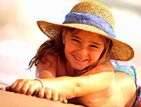 Little girl with hat lying on the beach in vacation.