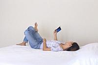 Female laying relaxing on bed holding up smart phone.