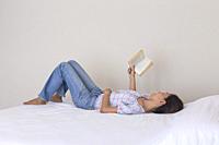 Female on a bed reading a book.