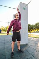 Fitness man warming up outdoors on sports ground and listen to music in headphones. Rotates body and swings hands.