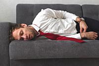 Tired overworked businessman deeply sleep on sofa. He slept all night on the couch in office clothes.