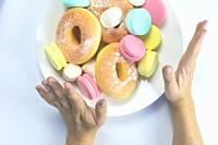 Woman hands making a hand sign of no and refuse for a white plate with fastfood and sugar, top view, healtcare and weightloss concept. donuts, macaron...