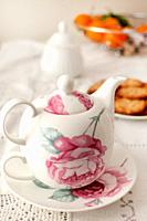 Biscuits on table, ready to be taken with tea. Teapot with floral motifs and various complementary elements.