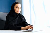 Beautiful woman with abaya dress working on her computer. Middle aged female employee at work in a business office in Dubai. Concept about middle east...