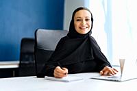 Beautiful woman with abaya dress working on her computer. Middle aged female employee at work in a business office in Dubai. Concept about middle east...