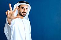 handsome man with dish dasha working in his business office of Dubai. Portraits of a successful businessman in traditional emirates white dress. Conce...