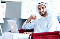 handsome man with dish dasha working in his business office of Dubai. Portraits of a successful businessman in traditional emirates white dress. Conce...