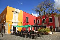 People sitting at an open-air cafe in front of the colorful colonial buildings in Barrio Del Artista district at the historic center, Puebla, Puebla S...