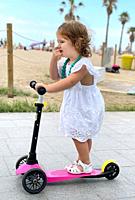 Little girl, playing with her scooter in the street.