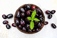 Dark pink-red ripe Syzygium cumini fruits. Dark black java plum in a wood bowl at isolated white background. Green mint leaf on top of some large java...