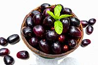 Dark pink-red ripe Syzygium cumini fruits. Dark black java plum in a wood bowl at isolated white background. Green mint leaf on top of some large java...