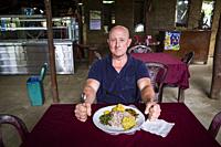 Tissa, Sri Lanka A tourist sits and eats a typical Sri Lankan meal of rice and curried vegetables with potatoes served on a plastic shee ton plate to ...