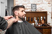 Man barber cutting hair of male client with clipper at barber shop. Hairstyling process. High quality photography.