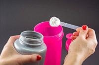 Sport, fitness, healthy lifestyle and people concept - close up of women with jar and bottle preparing protein shake.