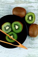 Black bowl with kiwis on wooden board.