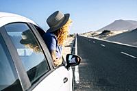Woman outside window car parked on a long asphalt road side during travel trip. Summer road trip concept with female traveler looking desert and mount...