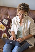 Adult young woman sit relax on couch using modern laptop browsing unlimited wireless internet, happy young people freelancer work on computer typing t...