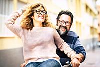 Happy adult mature beautiful couple enjoy and have fun riding a bike together - man carrying woman and laughing a lot - happy active people in leisure...
