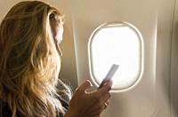 Young blond woman using smartphone on airplane.