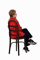 side back view of a full portrait of senior woman with shirt and pants sitting on chair on white background.