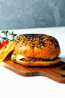 Cheeseburger with fries and cherry tomato on wooden board.