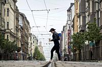 Riga, Latvia, A woman crosses tram tracks on a cobblestoned street with a cup of coffee.