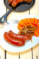 beef sausages cooked on iron skillet with carrot and onion.