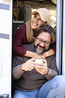 Portrait of man and woman adult couple sitting on the door of a camper van and enjoying travel holiday vacation. People on the road lifestyle van life...