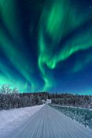 Northern light, aurora borealis in winter with snow, colorful with green and purple, among trees and a road in the forest, Gällivare, Swedish Lapland,...