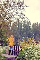 Young woman with yellow raincoat and rubber boots in spring nature.