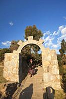 Indigenous woman in traditional dress passing through a stone arch and walking up to her house, Amantani Island, Titicaca Lake, Puno Region, Peru, Sou...