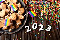 New year background of tray with gingerbread cookie men, rainbow flags and color sprinkles on wooden table.