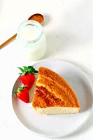 Jar with fresh milk on a white plate with a portion of lemon sponge cake with strawberries.