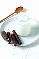 Jar with fresh milk on a white plate with chocolate wafer.