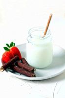 Jar with fresh milk on a white plate with chocolate wafer and strawberries.