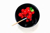 Cherries in syrup in black bowl on white background.