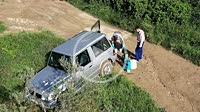 Two agriculturist people loading herbicide in a tank in a car next to land. Drone view. Bargota, Navarre, Spain, Europe.