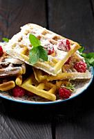 Stack of baked Belgian waffles with ripe red raspberry sprinkled with powdered sugar, breakfast.