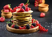 A stack of pancakes with fresh fruits poured with syrup on a black background.