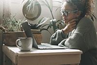 Serene woman work with notebook at home smiling at the display. Serene female use laptop indoor with plants in background. Green colours portrait of p...