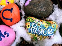 A painted Peace rock sits prominently amidst snow and other rocks with different colours and icons, Ontario, Canada. A message of peace and harmony fr...