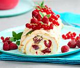 Baked meringue roll with red berries on a round plate, white background.