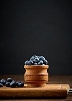 Ripe blueberries in a wooden bowl on the table, black background.