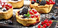 Fruit tart with red currants sprinkled with powdered sugar on a black table.