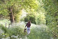 Jeune femme se promenant avec son chien sur un petit sentier de campagne borde d'ombelliferes en lisiere de foret, Departement d'Eure-et-Loir, region ...