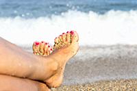 Woman feet closeup on a beach. Pink nails on toes. Enjoying sun on sunny summer day by the water.