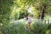 Young girl making a jump on a small country trail bordered by umbellifers on the edge of the forest, Eure-et-Loir department, Centre-Val-de-Loire regi...