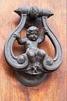 Old wrought iron knocker representing a child sitting on a swing on a wooden door.